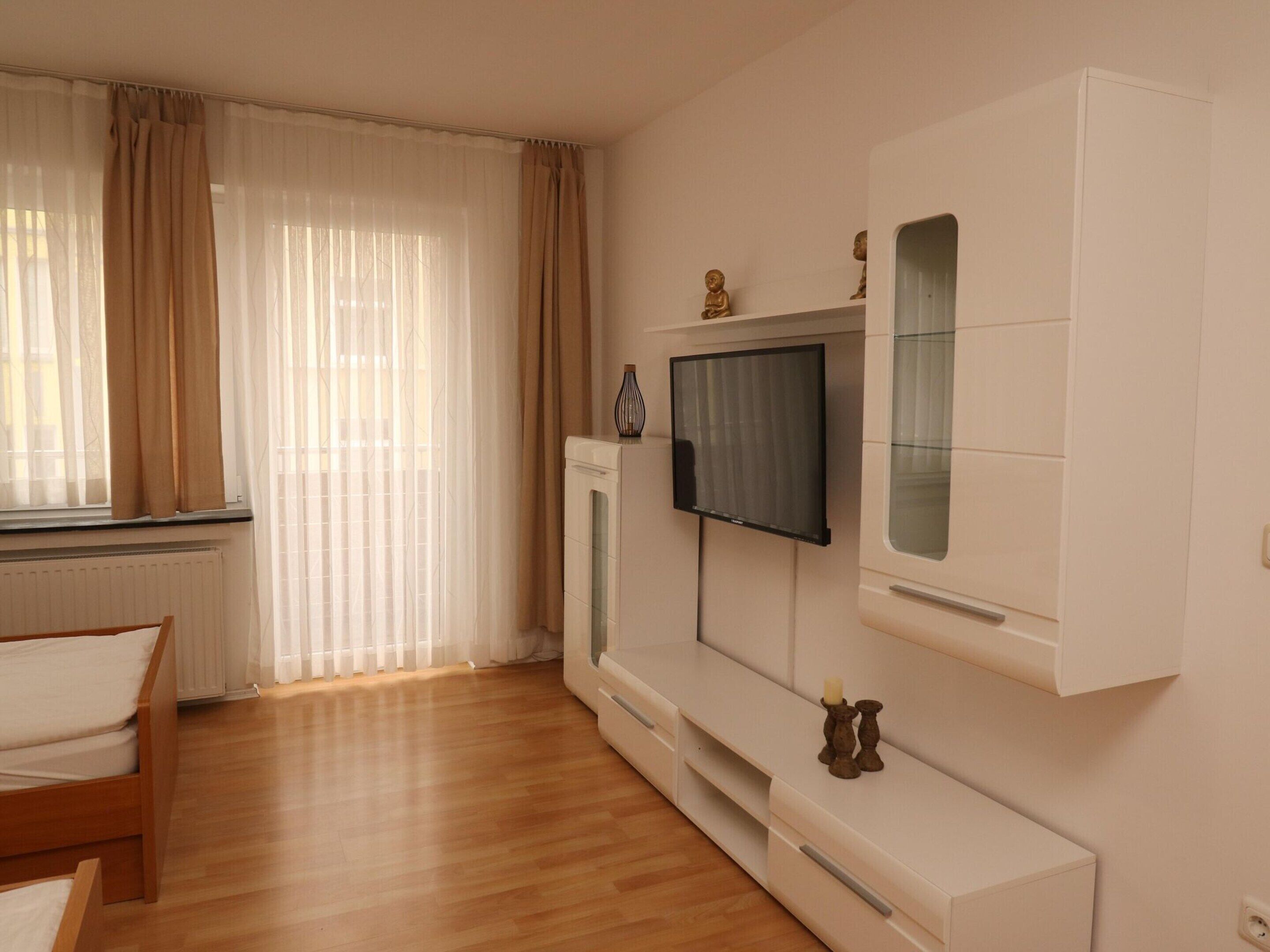 A modern living room with a wooden floor, a sofa, a TV mounted on the wall, and a radiator.