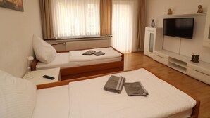 Habitación de hotel con dos camas, un televisor de pantalla plana, un radiador y una ventana con cortinas.
