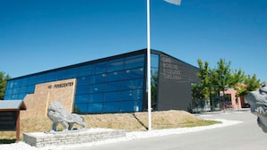 A modern building with a glass facade, a lion statue in front, and a flagpole with a flag.