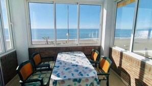 Een kamer met een tafel en stoelen, grote ramen met uitzicht op het strand en een bakstenen muur.