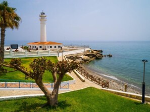 A coastal lighthouse with a white building nearby, a paved walkway, and a rocky shoreline. - Cozy Apartment in Torrox With Shared Pool (Torrox)