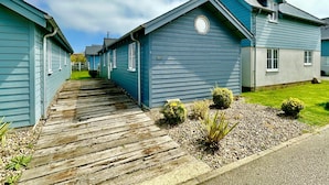 A row of blue houses with a wooden walkway leading to the entrance. - Stunning Coastal Beach House - Sleeping 4 in 2 Bedrooms - Pool and Beach Access Included. (Filey)