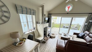 A cozy living room with a brown leather sofa, a dining table with a plaid tablecloth, and a fireplace. - Stunning Coastal Beach House - Sleeping 4 in 2 Bedrooms - Pool and Beach Access Included. (Filey)