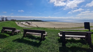 A beach with two wooden benches facing the ocean, a clear sky, and a distant shoreline. - Holiday Home in Scherpenisse Near the Sea (Scherpenisse)