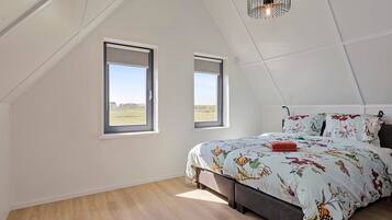 Un dormitorio con techo inclinado, dos ventanas, una cama con ropa de cama floral y una lámpara colgante.