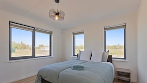 A bedroom with a bed, two windows, a small bedside table, and a hanging light fixture. - Holiday Home in Scherpenisse Near the Sea (Scherpenisse)