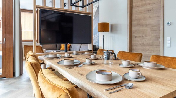 A modern dining area with a long wooden table set for a meal, surrounded by comfortable seating. - Apartment in Schruns Near Silvretta Ski Area (Schruns)