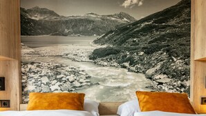Ein Schlafzimmer mit großem Fenster und Blick auf eine gebirgige Landschaft mit Fluss.