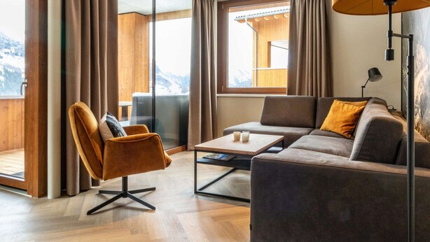 Ein modernes Wohnzimmer mit einer Couch, einem Sessel, einem Couchtisch und einem großen Fenster mit Vorhängen.