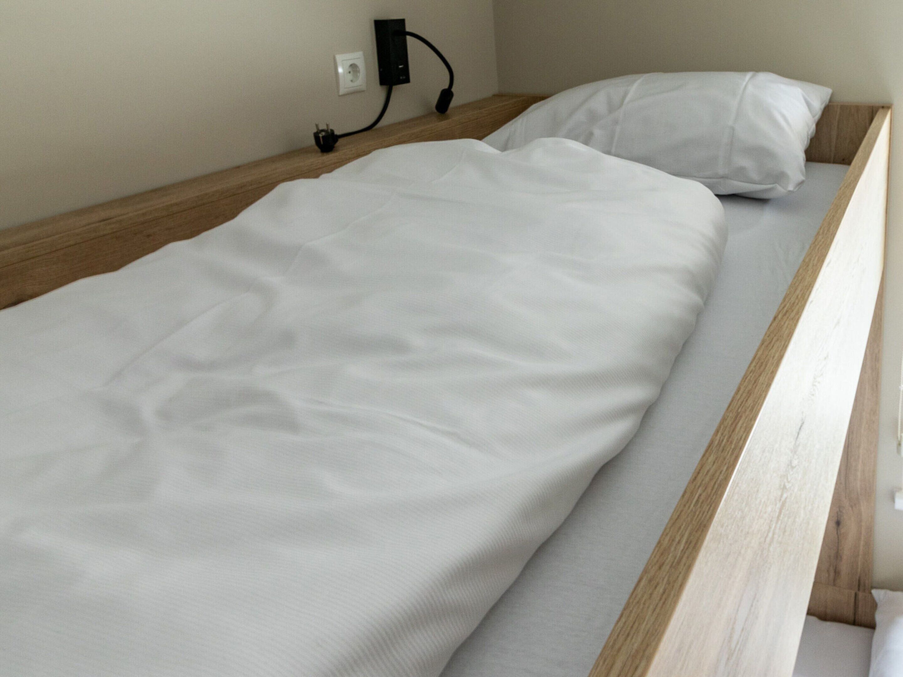 Una cama individual con ropa de cama blanca en una habitación con cabecera de madera y un enchufe de pared.