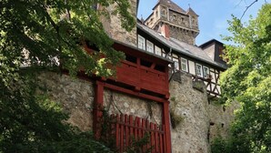 A historic building with a stone facade, a red wooden gate, and a tower with a weather vane. - Apartment in Geiersthal (Weilmünster)