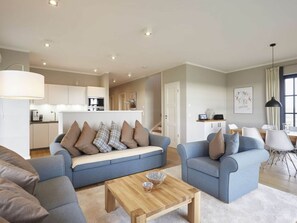 A modern living room with a sofa, two armchairs, and a coffee table. A kitchen is visible in the background. - Luxury Roof Villa With Sauna and Fireplace (Dranske)