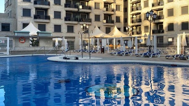 A swimming pool with lounge chairs and umbrellas, surrounded by a high-rise building with balconies. - Belvilla by OYO Apartment in Fuengirola (Fuengirola)