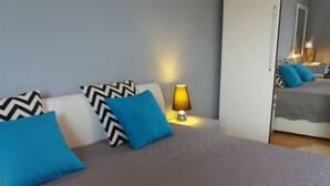 Un lit bien fait, avec des oreillers bleus et noirs, une lampe de chevet et un miroir qui reflète la pièce.