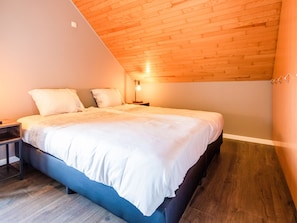 A bedroom with a sloped ceiling, a bed with white bedding, a nightstand, and a lamp. - Holiday Home in Haringe for ten Person (Poperinge)