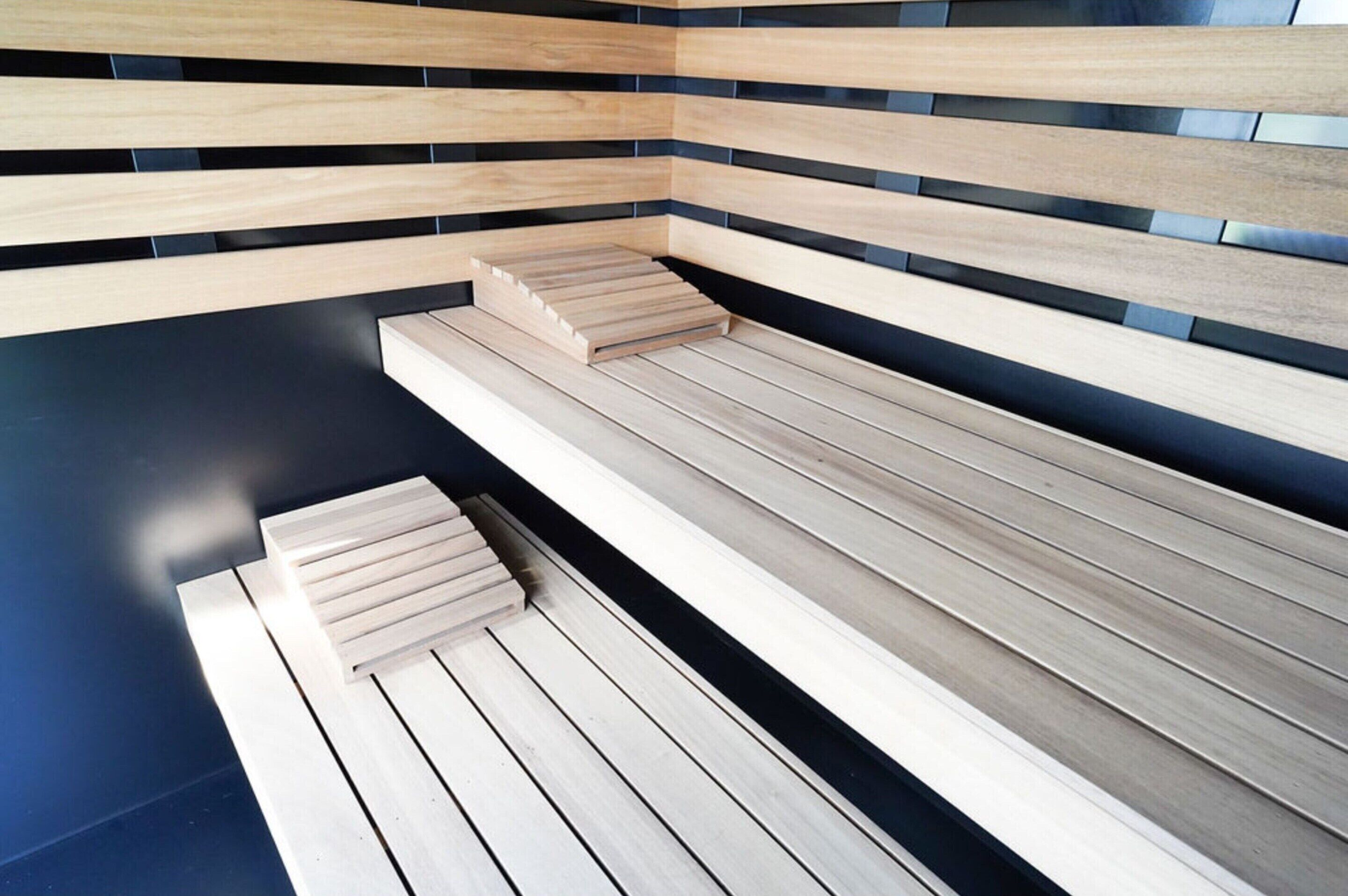 Eine moderne Sauna mit Holzbänken und schwarzen Fliesenwänden.