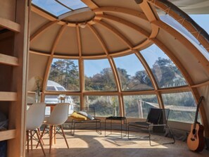 A spacious, dome-shaped room with large windows, a guitar, and a table with chairs. - Starlit Tent Lodge Escape (Zuna)
