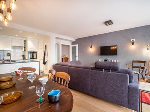 A modern living room with a grey sofa, a dining table with plates and glasses, and a kitchen in the background. - Apartment Near Ostend With Sea View (Koksijde)