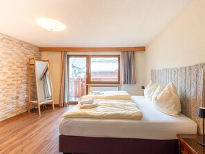 Habitación de hotel con una cama, piso de madera, una ventana con cortinas y vista a un edificio.
