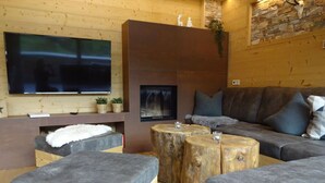 Uma sala de estar moderna com uma TV de tela plana, uma lareira e um espaço de estar acolhedor com um sofá e pufes.