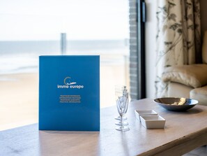 A blue booklet titled "Immo Europe" on a wooden table with a glass of water, a bowl, and a small white box. - Apartment in St-idesbald With Sea View (Koksijde)