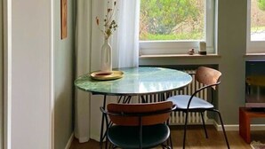 A dining area with a round table, two chairs, a vase with flowers, and a window with curtains. - Trappen Comfortable Holiday Residence (Birresborn)