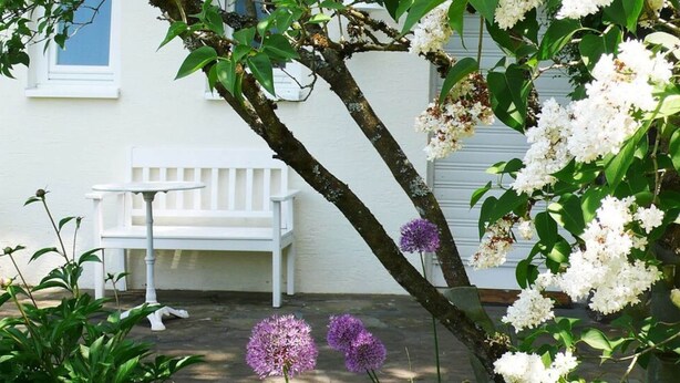 A white bench and table outside a building with white walls and a window. - Trappen Comfortable Holiday Residence (Birresborn)