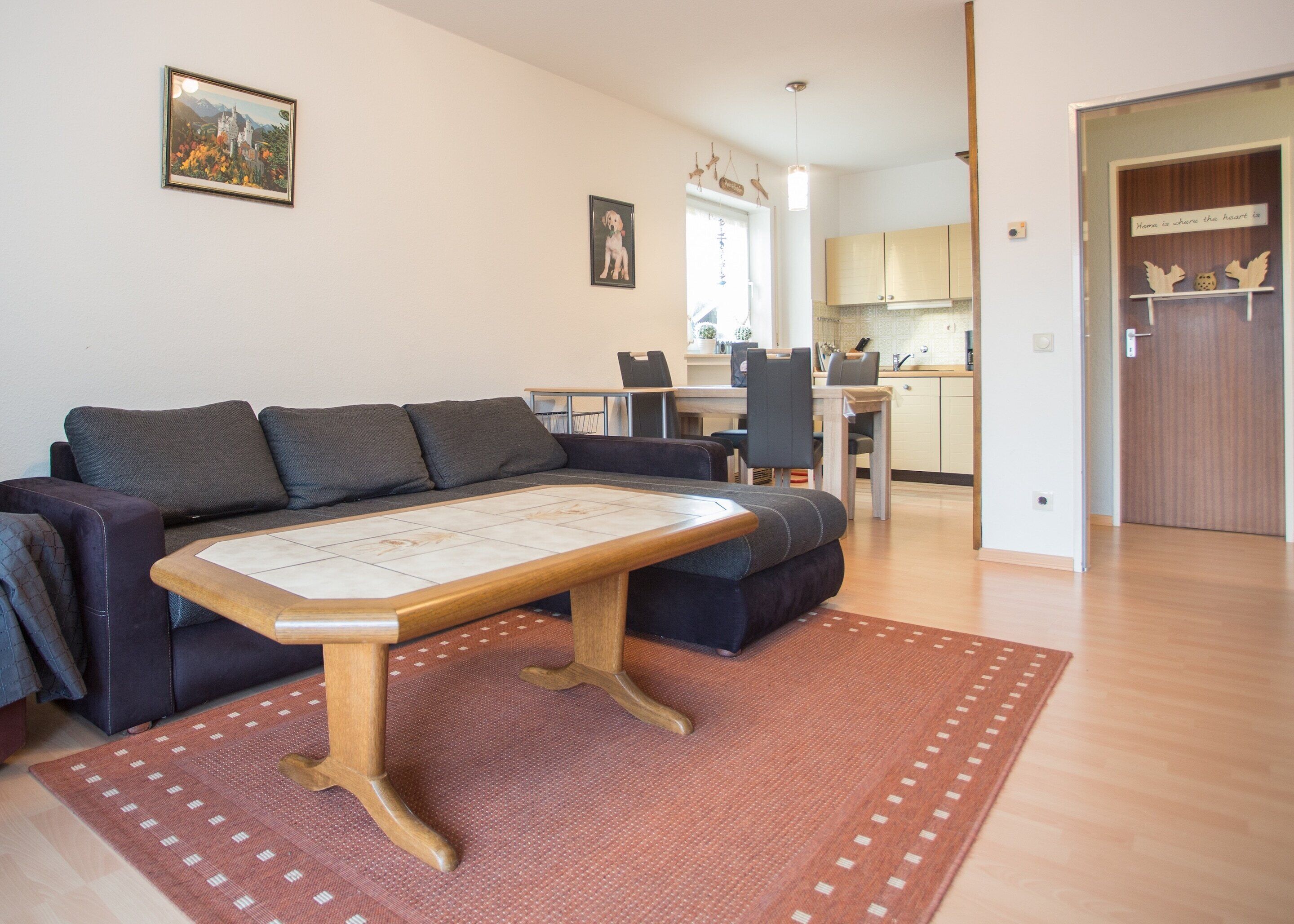 A living room with a sofa, a coffee table, and a rug. There is a kitchen in the background.