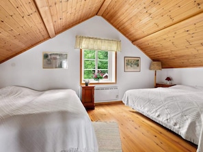 Een slaapkamer met twee bedden, een raam met uitzicht op groen en een radiator.