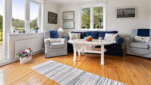 A room with a wooden floor, a white table, two sofas, and a chandelier. - 5 Star Holiday Home in Stromstad (Stromstad)