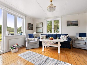 Quarto com piso de madeira, uma mesa branca, dois sofás e um candelabro.