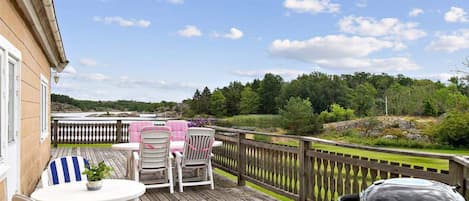 A wooden deck with outdoor furniture, a barbecue grill, and a view of a river and forest.
