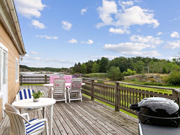 A wooden deck with outdoor furniture, a barbecue grill, and a view of a river and forest.
