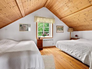 A bedroom with two beds, a window with a view of greenery, and a radiator.