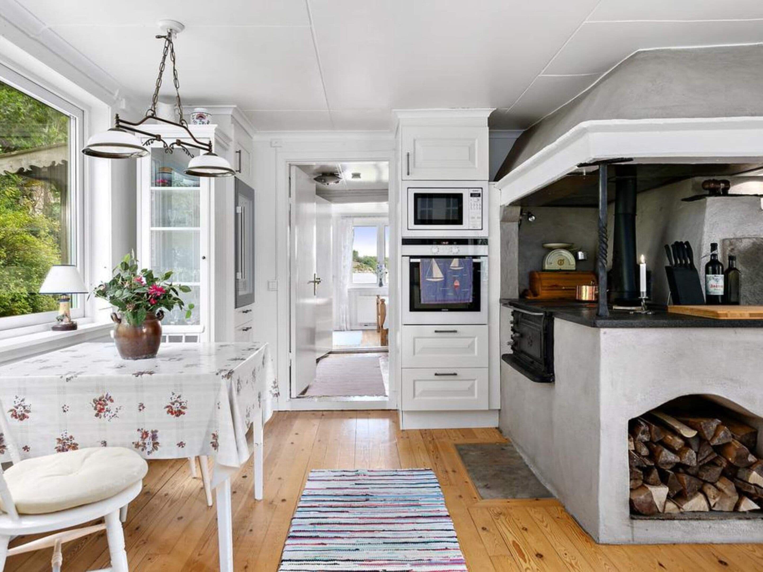 A modern kitchen with white cabinetry, a built-in oven, a microwave, and a stone fireplace.