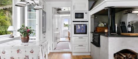 A modern kitchen with white cabinetry, a built-in oven, a microwave, and a stone fireplace.