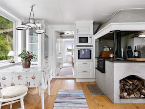 A modern kitchen with white cabinetry, a built-in oven, a microwave, and a stone fireplace. - 5 Star Holiday Home in Stromstad (Stromstad)