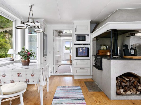A modern kitchen with white cabinetry, a built-in oven, a microwave, and a stone fireplace.