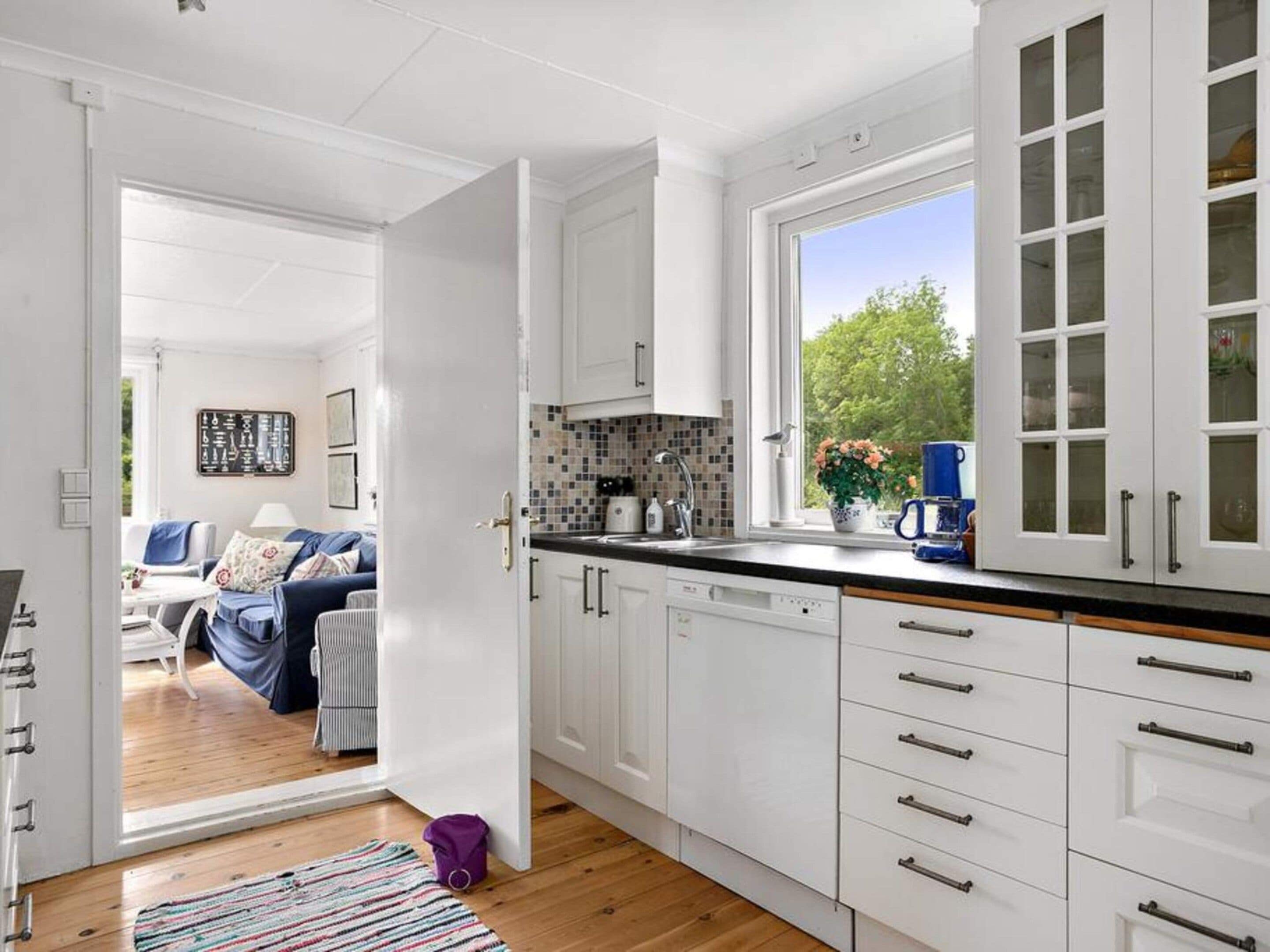 A modern kitchen with white cabinets, a black countertop, and a window with a view of greenery.