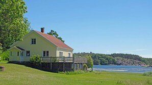 A yellow house with a red roof, a deck, and a view of a lake and forest. - 5 Star Holiday Home in Stromstad (Stromstad)