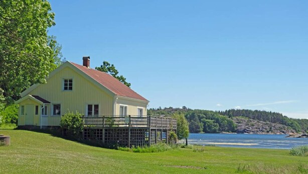 Una casa gialla con tetto rosso, una veranda e vista su un lago e una foresta.