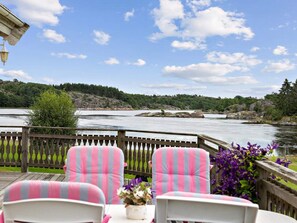 A deck with two striped chairs and a table, overlooking a river with a wooden railing.