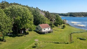 Una casa con veranda, immersa in un prato curato e alberi, vicino a un corso d'acqua.