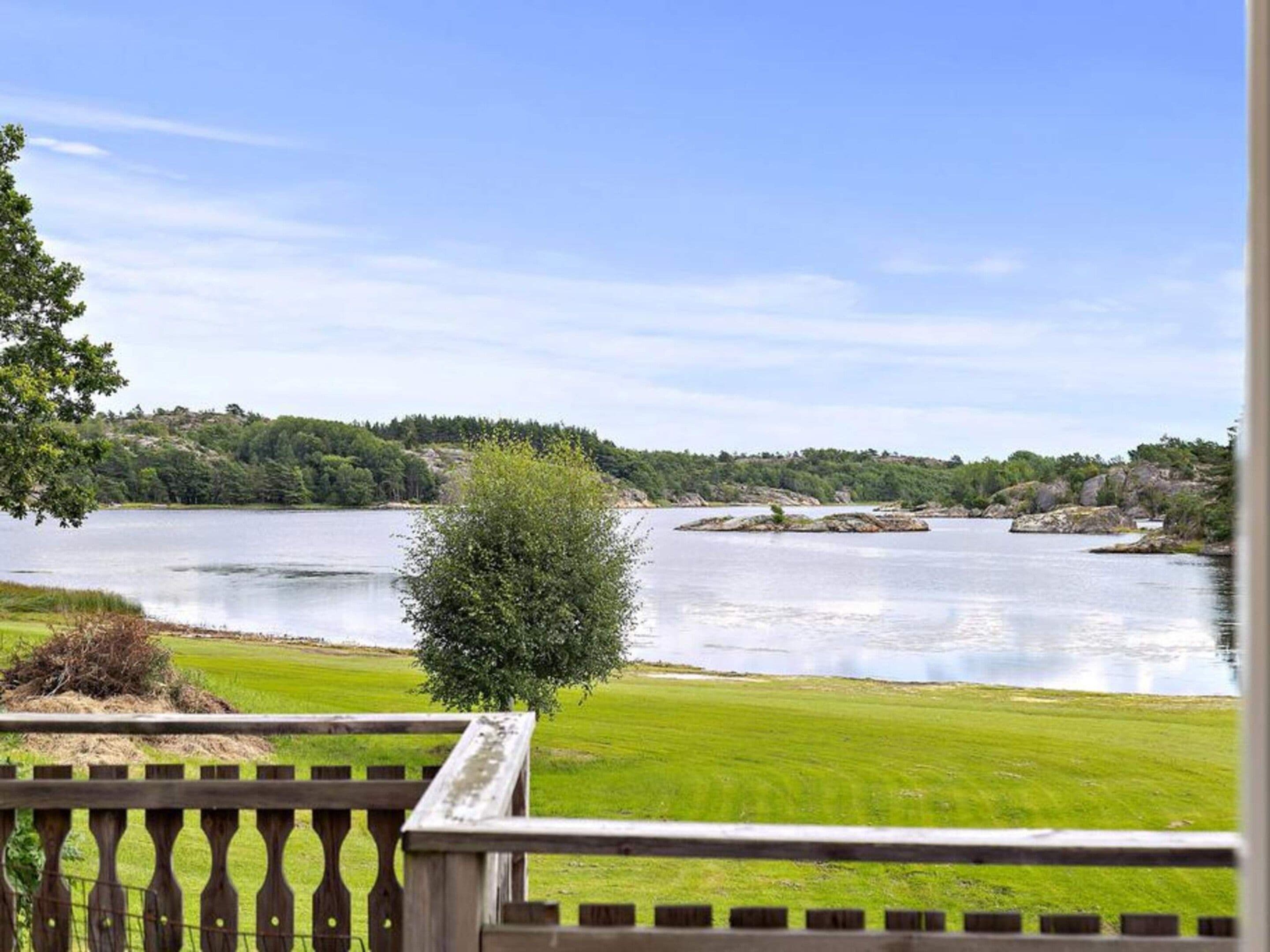 A view of a lake with a grassy area and a wooden fence in the foreground.