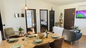 A dining area with a wooden table set for four, surrounded by chairs. There is a sofa and a television mounted on the wall. - Villa in Malaga, Private Pool and sea View (Cartama)