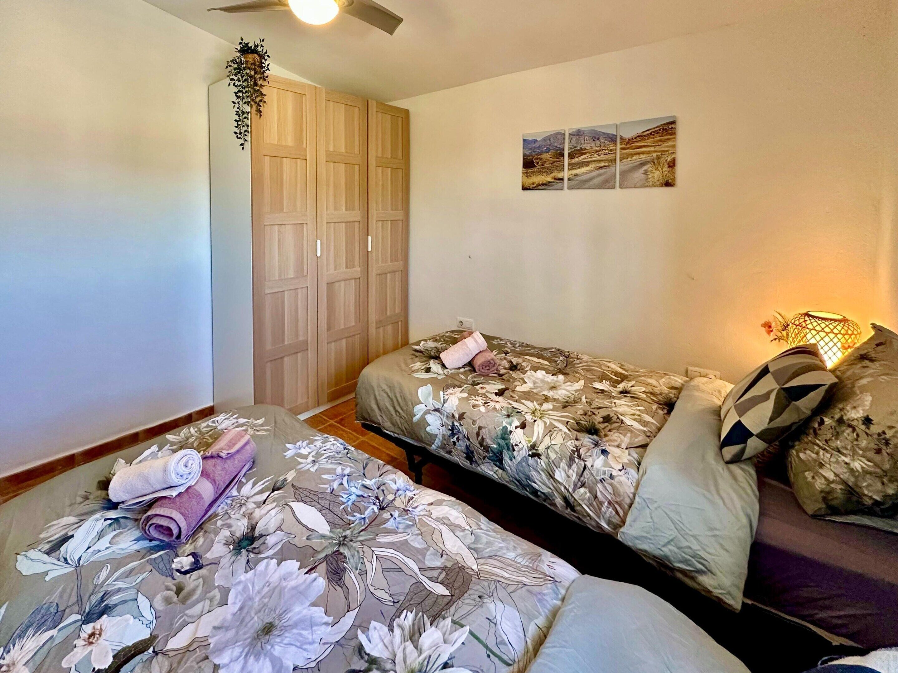 Ein Schlafzimmer mit zwei Betten, einem Kleiderschrank, einem Deckenventilator und einem Wandbild.