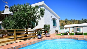 A swimming pool with a wooden deck, potted plants, and a white building with a tiled roof. - Villa in Malaga, Private Pool and sea View (Cartama)