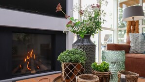 A modern living room with a fireplace, a large vase with flowers, and wicker candle holders on a wooden table. - Villa in Friesland With Sauna and Jetty (Delfstrahuizen)