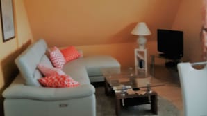 Uma sala de estar com um sofá, uma mesa de centro, uma luminária e uma televisão.