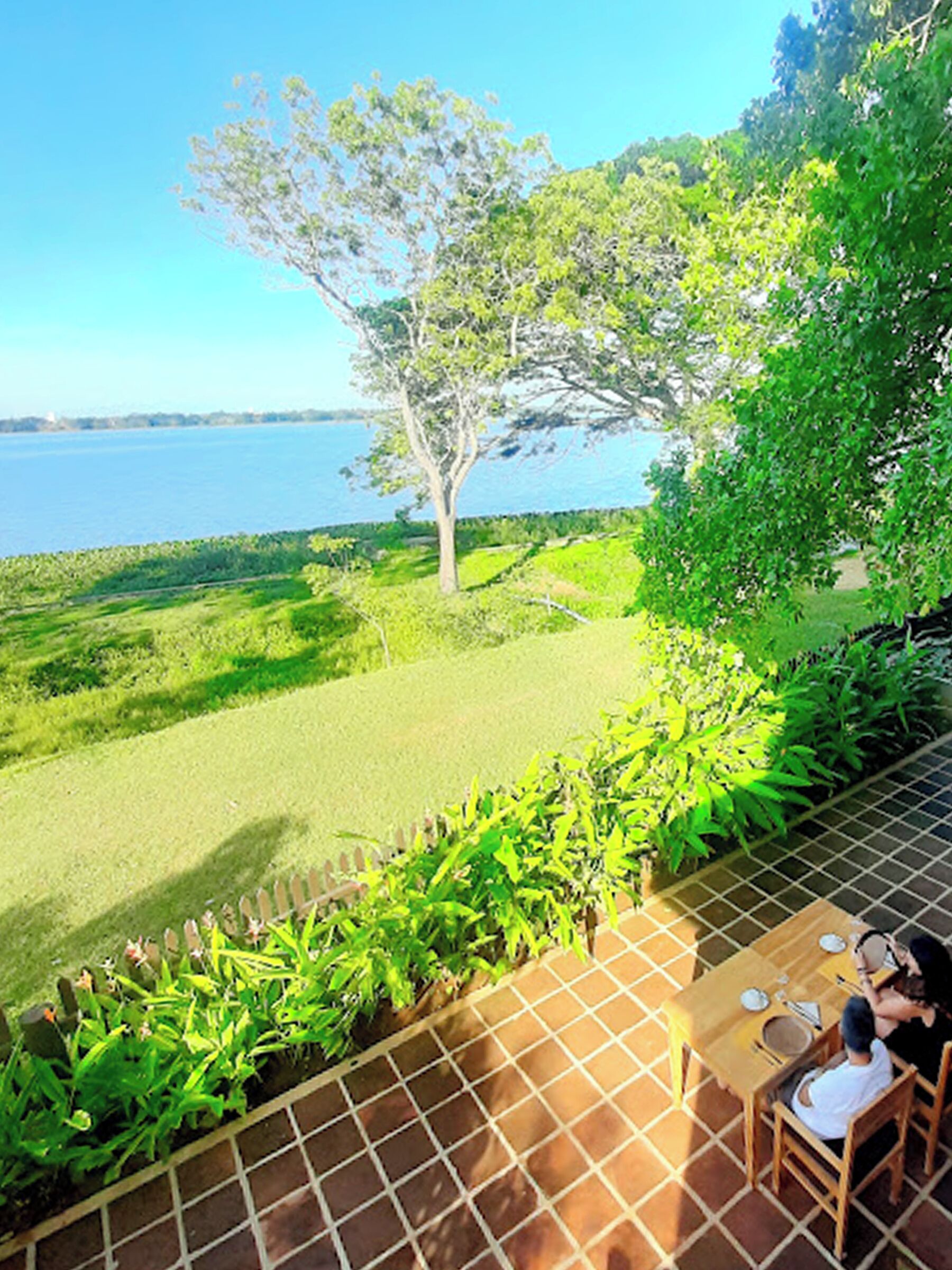 A dining area with a view of a lake, surrounded by greenery and a tiled patio.